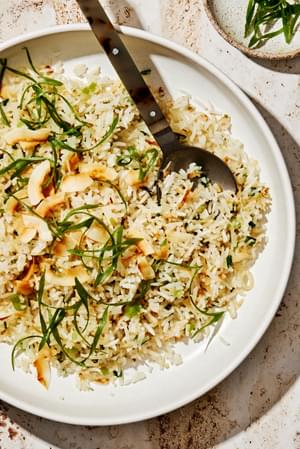 homemade coconut fried rice with green onions, ginger, and sweetened coconut flakes in a serving bowl with a wooden spoon