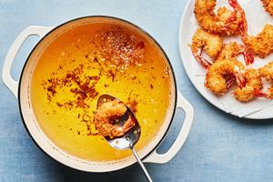 homemade coconut shrimp being fried in vegetable oil in a pot and scooped out to cool on a paper towel lined plate