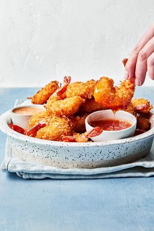 a plate of homemade coconut shrimp being dipped into homemade curry sauce and ginger mayo