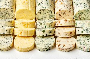 5 sticks of compound butters lined up and sliced made with fresh herbs, citrus zest and juice and caramelized onions