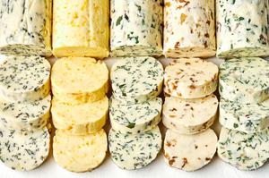 5 sticks of compound butters lined up and sliced made with fresh herbs, citrus zest and juice and caramelized onions