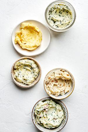 5 bowls of softened homemade compound butters made with fresh herbs, citrus zest and juice and caramelized onions