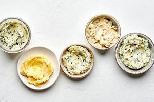 5 bowls of softened homemade compound butters made with fresh herbs, citrus zest and juice and caramelized onions