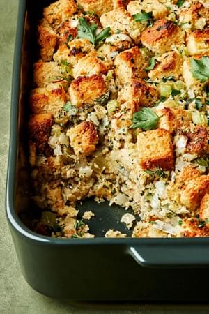 cornbread stuffing in a casserole dish topped with fresh parsley with a scoop taken out