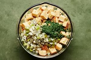 broken cornbread pieces, parsley and cooked onion and celery being mixed together in a bowl for cornbread stuffing