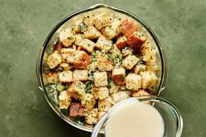 chicken stock whisked with eggs being poured overtop of cornbread stuffing in a large mixing bowl
