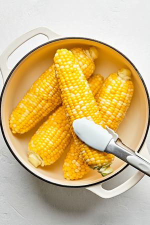 corn on the cob cooked in a pot of boiling water being removed with tongs to transfer to a serving platter