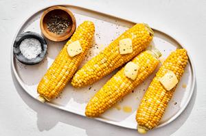 4 homemade corn on the cob on a platter topped with butter beside small bowls of salt and pepper for serving