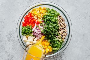 orange juice being poured into a bowl with the other cowboy caviar ingredients including black eyed peas, corn & bell pepper
