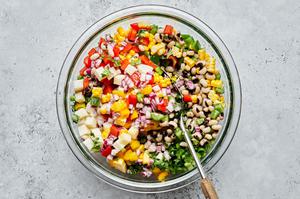 homemade cowboy caviar being stirred together in a large mixing bowl made with jicama, bell pepper, corn and black eye peas