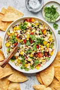 homemade cowboy caviar in a serving bowl with a spoon surrounded by tortilla chips and bowls of salt and cilantro