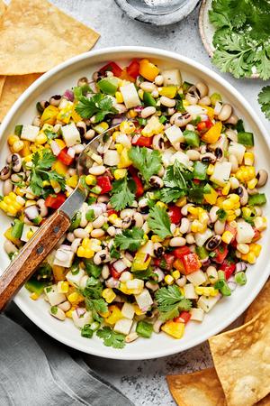 homemade cowboy caviar in a serving bowl with a spoon surrounded by tortilla chips and bowls of salt and cilantro