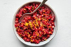 cranberry relish being stirred in a bowl made with cranberries, orange, apples, sugar, salt and lemon juice