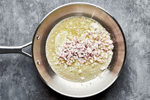 chopped shallot being cooked in melted butter in a skillet to make rich and creamy creamed spinach