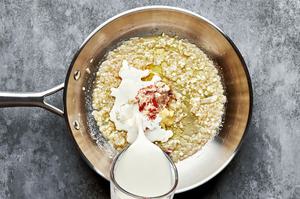 heavy cream being poured in a skillet with shallot, butter, garlic, dijon, salt, pepper, garlic powder, nutmeg and cayenne