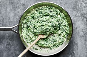 creamed spinach being stirred in a skillet with a wooden spoon made with butter, cream, dijon, spices and parmesan cheese