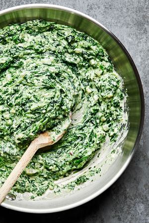 creamed spinach being stirred in a skillet with a wooden spoon made with butter, cream, dijon, spices and parmesan cheese