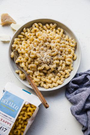 homemade Creamy Cavatappi in a bowl with a fork next to a linen napkin and a bag of DeLallo Cavatappi pasta