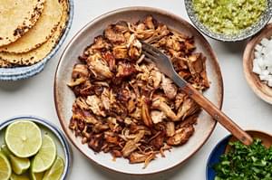 crispy pork carnitas, corn tortillas, salsa verde, onion, cilantro and lime wedges in bowls to make crispy carnitas tacos