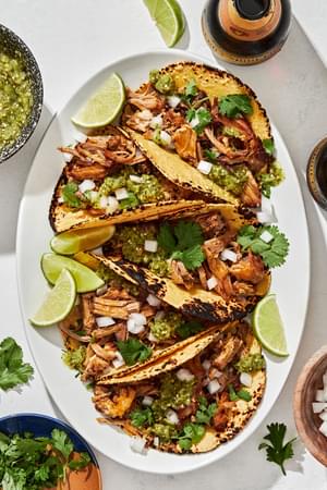 crispy carnitas tacos in homemade corn tortillas topped with onion, cilantro and salsa verde served with lime wedges