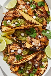 crispy carnitas tacos in warmed corn tortillas topped with onion, cilantro and salsa verde served with lime wedges