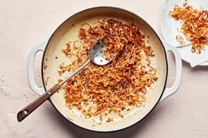 crispy fried shallots in a skillet being scooped out with a slotted spoon onto a paper towel lined plate