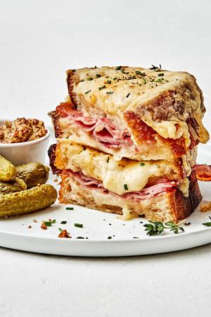 a homemade croque monsieur sandwich stacked on a plate served with pickles and stone ground mustard