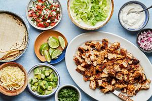 chicken taco fixing in bowls including chicken, tortillas, lettuce, cheeses avocado, pico, cilantro, onion and sour cream
