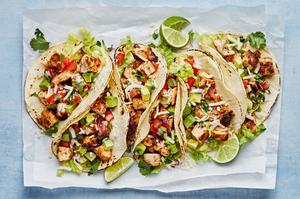 chicken tacos on corn tortillas topped with pico, cheese, lettuce and avocado on a sheet of parchment paper