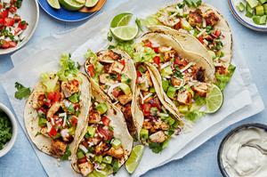 chicken tacos on corn tortillas topped with pico, cheese, lettuce and avocado on a sheet of parchment paper