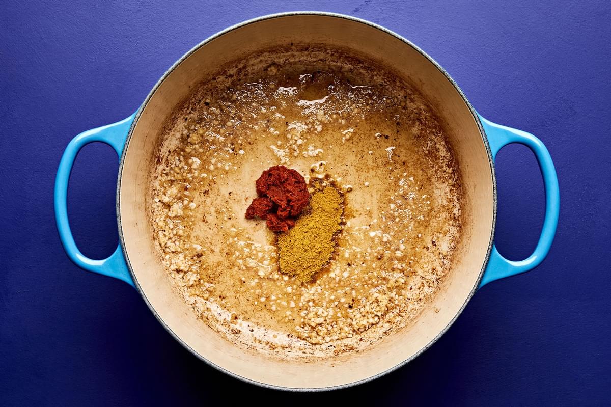 garlic, ginger, red curry paste, and yellow curry powder being cooked in sesame oil in a pot