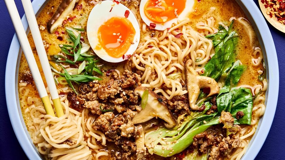 A bowl of curry ramen with noodles, and vegetables submerged in a golden curry broth topped with soft boiled eggs
