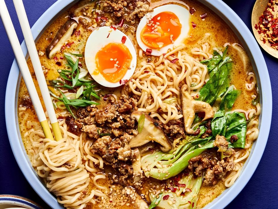 A bowl of curry ramen with noodles, and vegetables submerged in a golden curry broth topped with soft boiled eggs