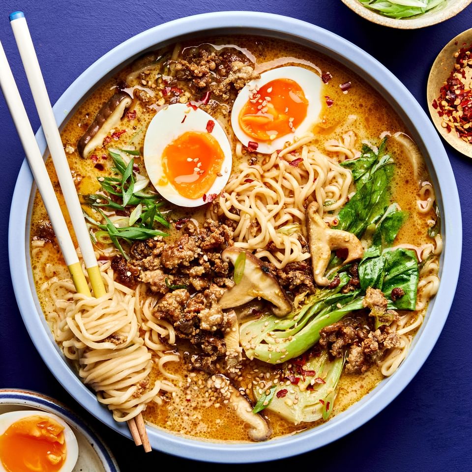 A bowl of curry ramen with noodles, and vegetables submerged in a golden curry broth topped with soft boiled eggs