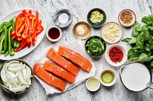 Ingredients for one pot curry salmon including raw salmon, bell peppers, onions, garlic, cilantro, basil, and curry paste