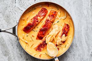 Coconut Curry broth in a large skillet with four filets of salmon and coconut curry being spooned over the salmon.