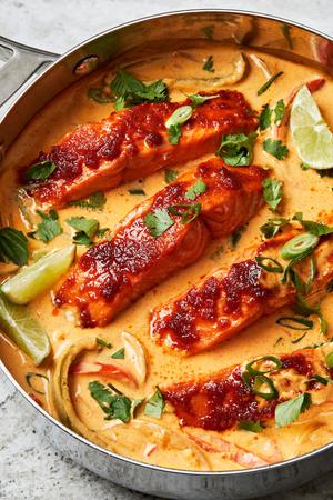 Four salmon filets in a coconut curry broth with bell peppers and onions topped with cilantro and basil and fresh limes