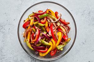 peppers & onions in a glass bowl being marinaded in olive oil, lime juice, taco seasoning, soy sauce, and cilantro