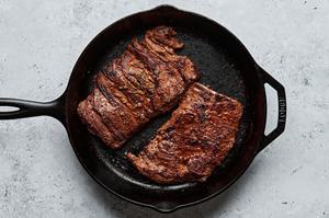 flank steak coated in olive oil, lime juice, taco seasoning, soy sauce, and cilantro being cooked in a cast iron skillet