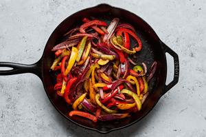 peppers and onions marinaded in olive oil, lime juice, taco seasoning, soy sauce, and cilantro being cooked in a skillet