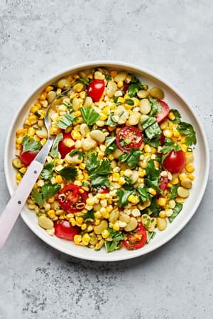 a bowl of easy succotash made with corn, lima beans, tomatoes, green onions, cilantro, basil, lime juice salt & pepper