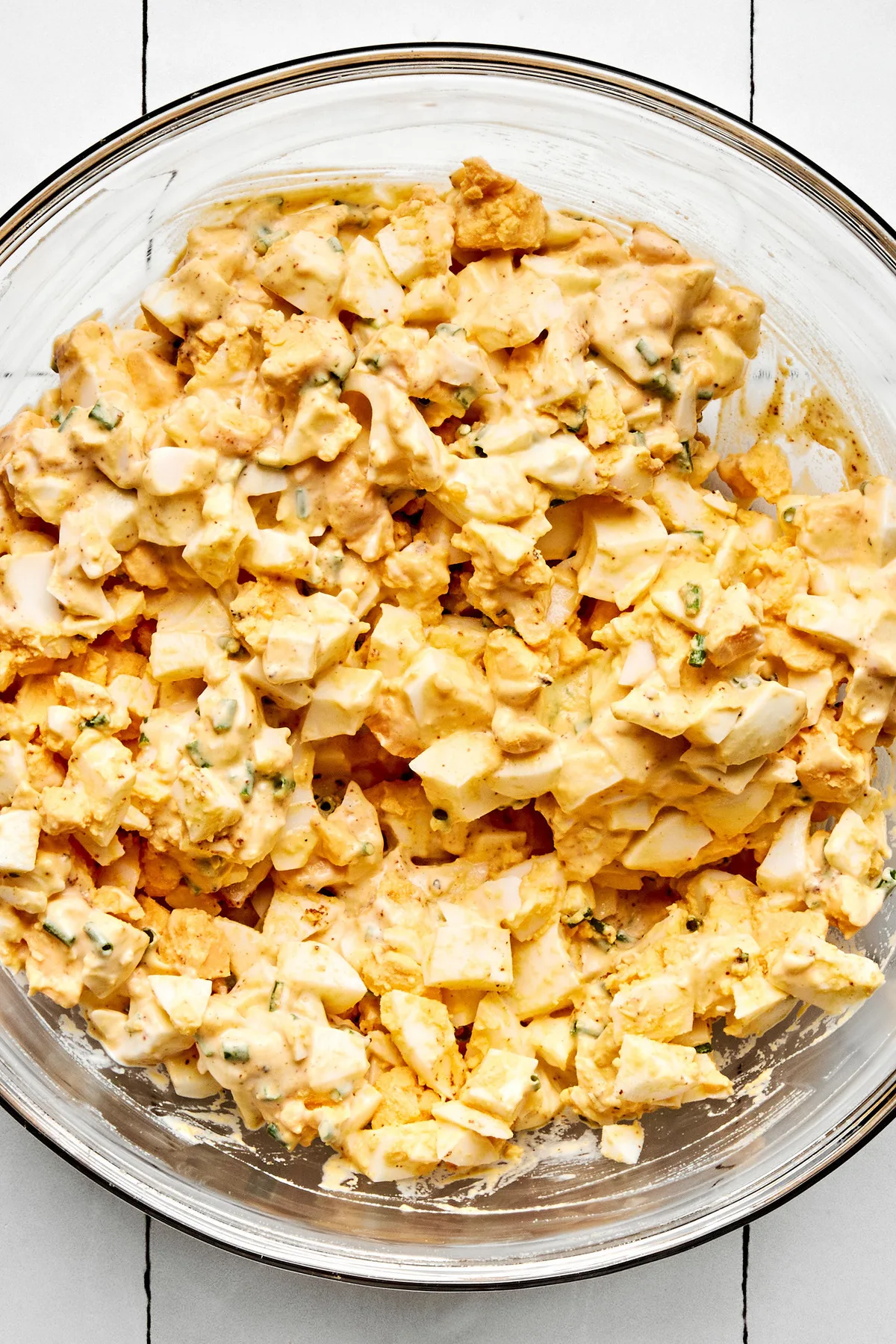 a bowl of creamy egg salad sandwich filling made with, chopped boiled egg, mayo, dijon, pickle juice, chives and spices