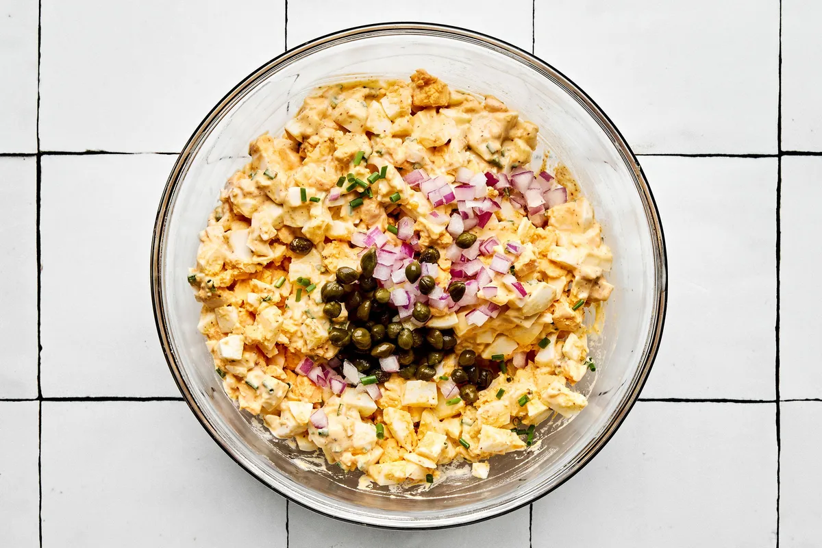 finely diced red onion and capers being mixed into to creamy egg salad sandwich filling