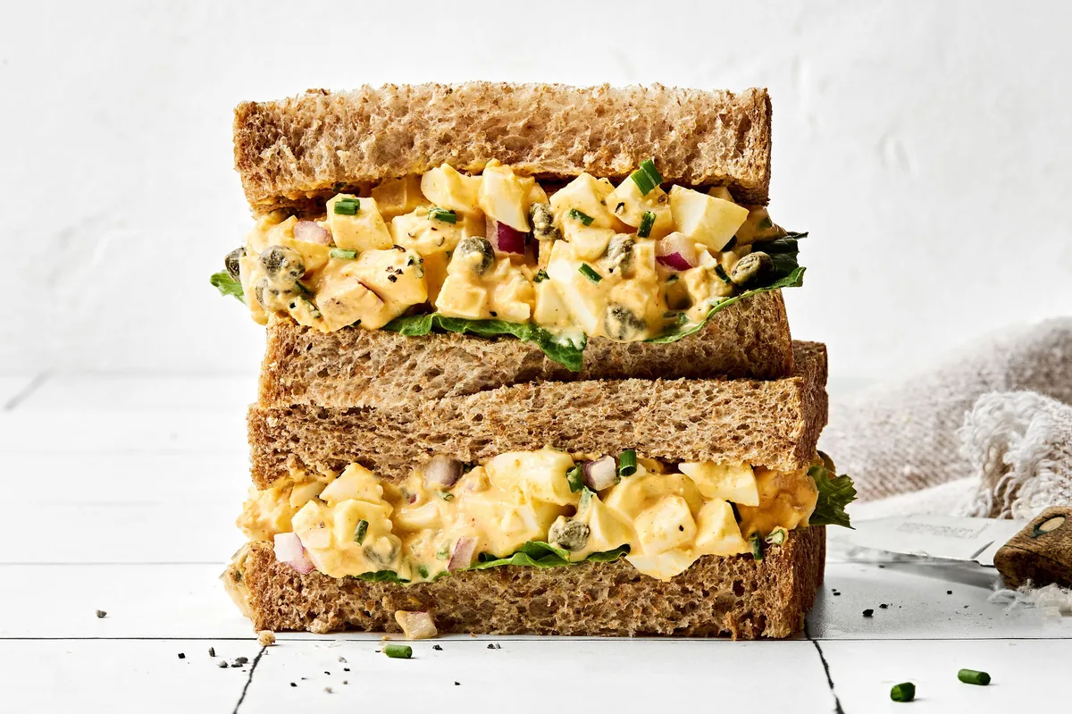 A homemade Egg salad sandwich sliced in half and stacked, showing creamy filling between soft bread slices, ready to eat.