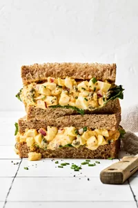 A homemade Egg salad sandwich sliced in half and stacked, showing creamy filling between soft bread slices, ready to eat!