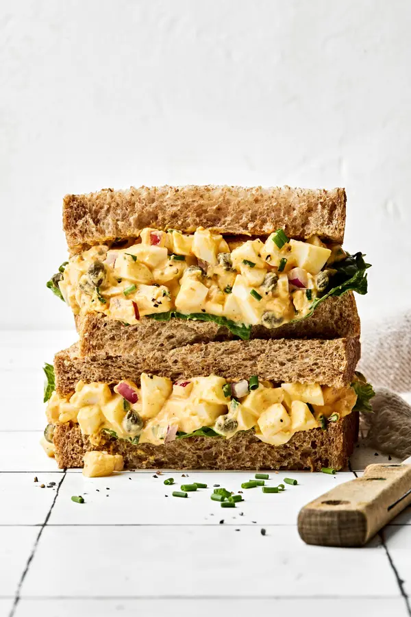 A homemade Egg salad sandwich sliced in half and stacked, showing creamy filling between soft bread slices, ready to eat!