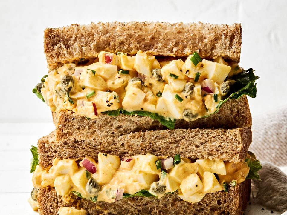 A homemade Egg salad sandwich sliced in half and stacked, showing creamy filling between soft bread slices, ready to eat!