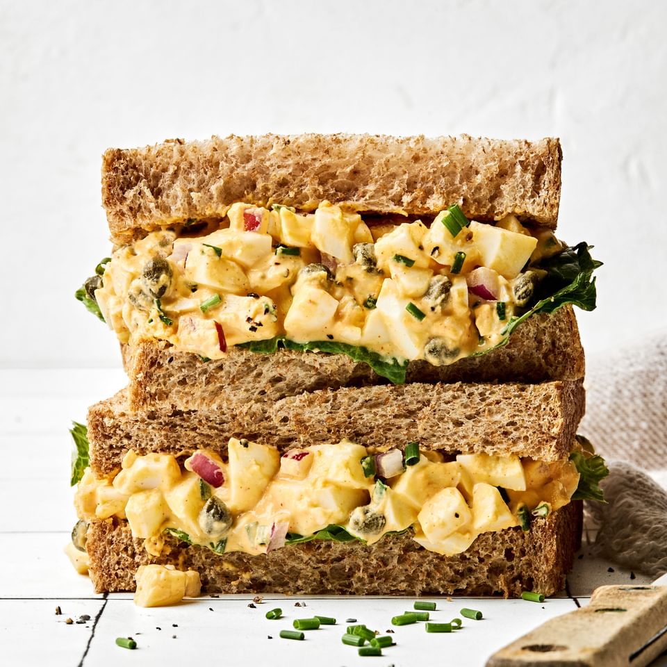 A homemade Egg salad sandwich sliced in half and stacked, showing creamy filling between soft bread slices, ready to eat!
