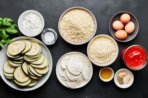 Ingredients for eggplant parmesan shown in small bowls including eggplant, mozzarella, parmesan, marinara, eggs and panko.
