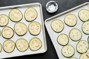 Eggplant slices on two parchment lined baking sheets seasoned with kosher salt.
